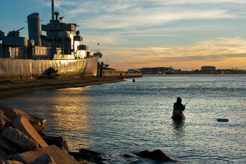 Fisherman fishing at Seawolf Park with USS Stewart to his left.